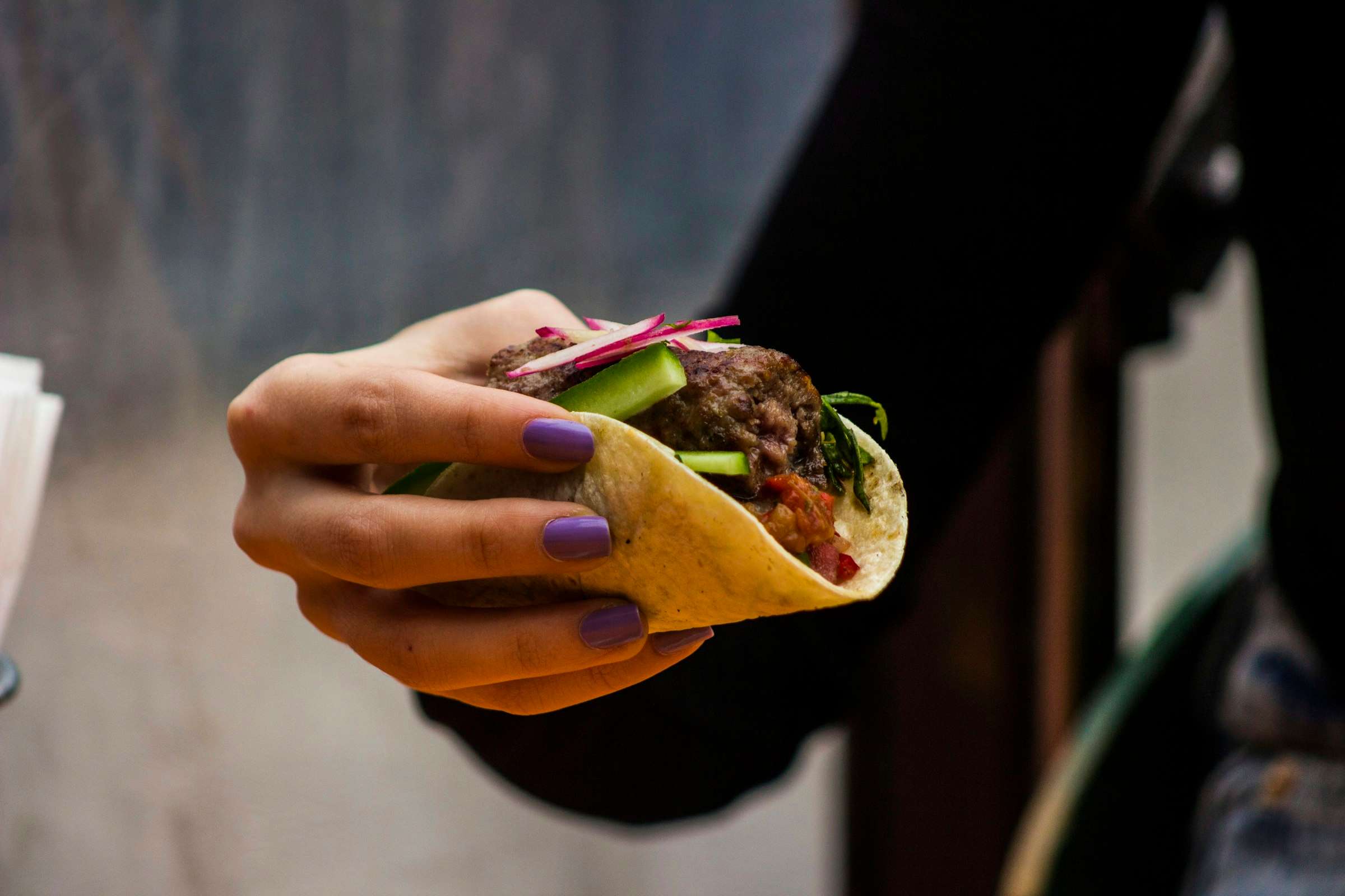 Hand hält einen Taco vor dunklem Hintergrund